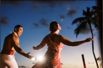 Two people dancing under evening sky with palm trees and warm lighting.