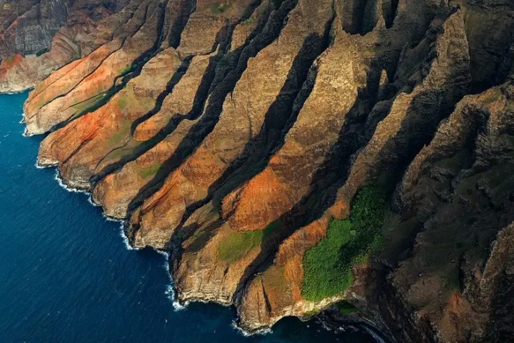 Aerial view of rugged, colorful cliffs meeting the ocean.