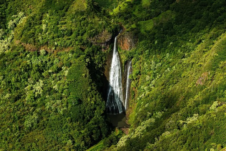 Aerial view of a waterfall cascading down green cliffs into a small pool.