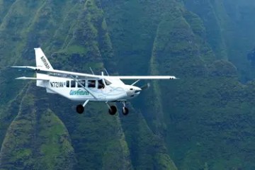 Small airplane flying over green, mountainous terrain.