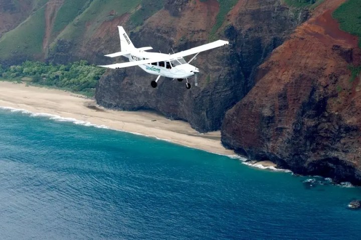Small plane flying over a coastal landscape with cliffs, beach, and ocean.