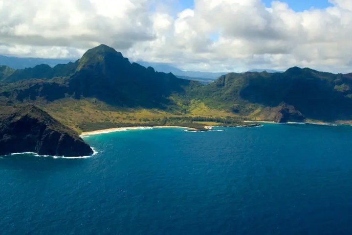 Aerial view of a lush, mountainous coastline with a beach and blue ocean.