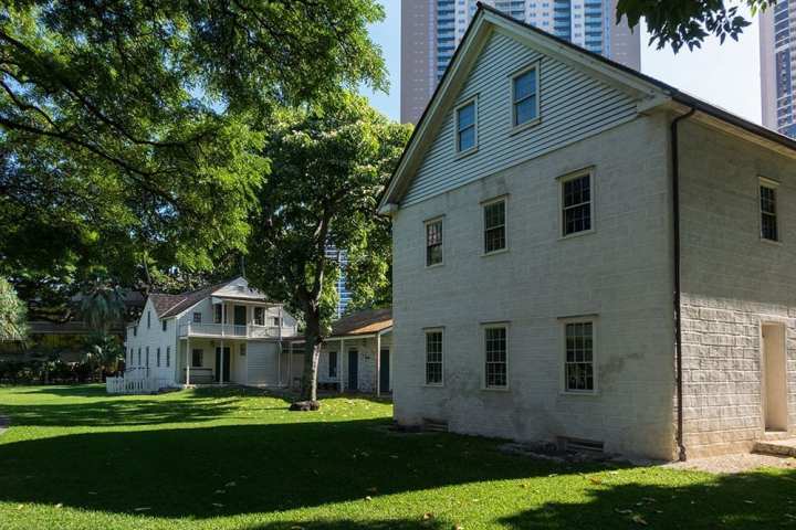 a large brick building with grass in front of a house with Mission Houses Museum in the background