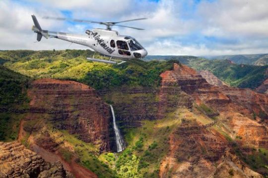 a helicopteron a rock with Waimea Canyon State Park in the background
