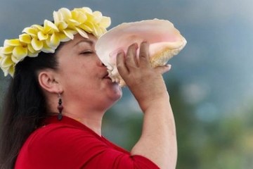 a woman blowing a hawaiian shell