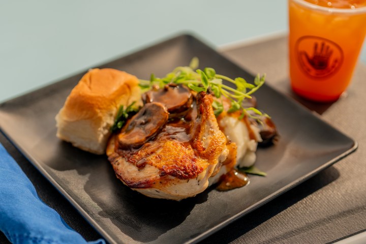 Grilled chicken with mushrooms, mashed potatoes, a roll, and a drink on a black plate.