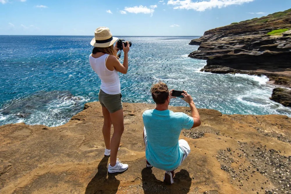 Two people on a rocky cliff photographing the ocean with cameras.