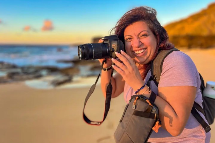 Smiling person with a camera on a sunny beach holding a camera.