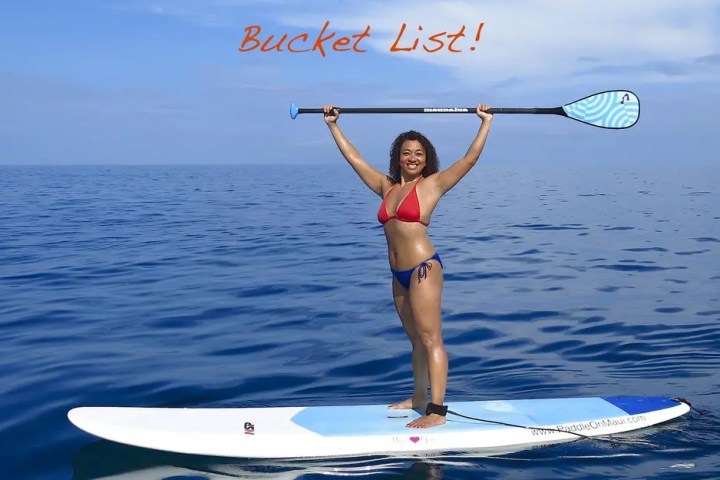 Person in a red bikini on a paddleboard, holding a paddle above their head in ocean.