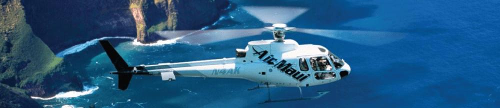 Helicopter flying over blue ocean near rocky coastline with green cliffs.