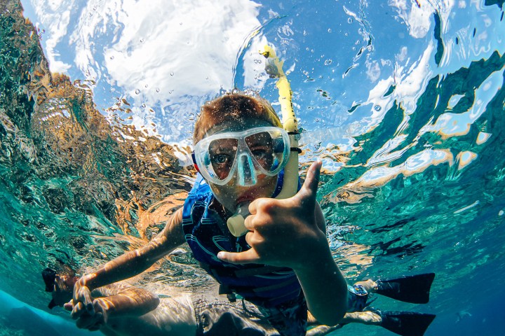 Child snorkeling under water with goggles and snorkel, giving thumbs-up.