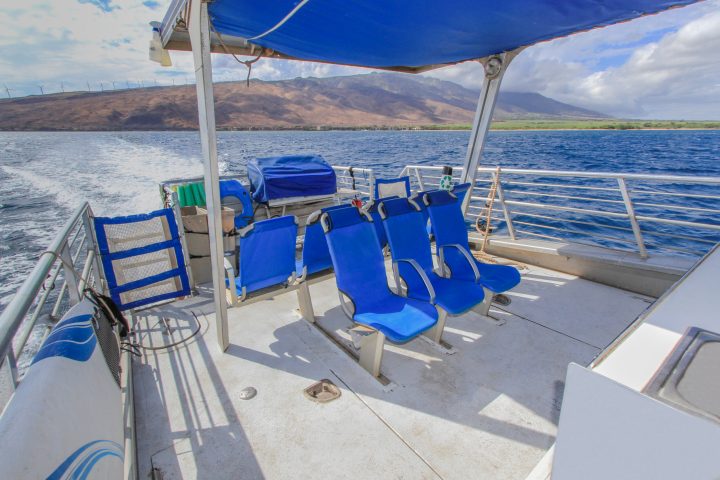 Empty blue seats on a boat with ocean and mountain views.