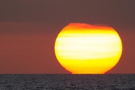 Large sun setting over the ocean with a dark sky above.