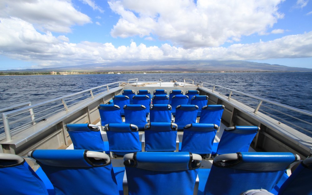 Empty boat deck with blue seats facing ocean, cloudy sky.