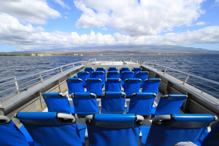 Empty boat deck with blue seats facing ocean, cloudy sky.