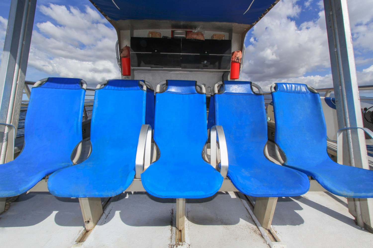 Five blue seats on a boat deck under a cloudy sky.