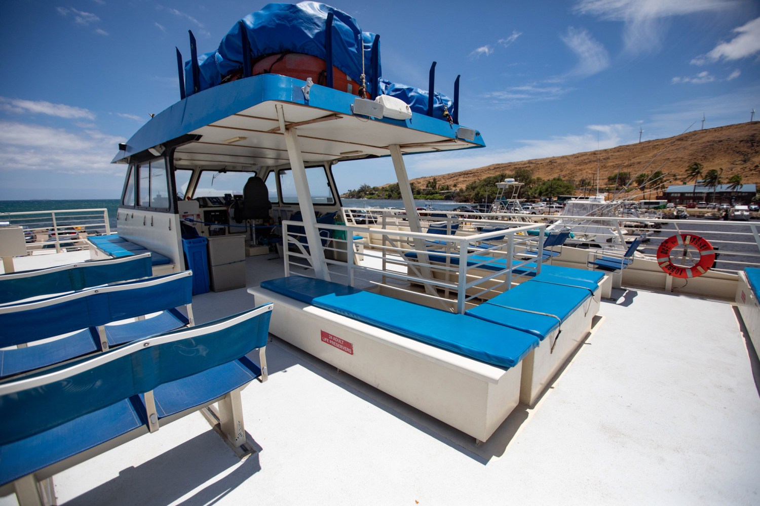 Open upper deck of a boat with blue benches and a clear sky.