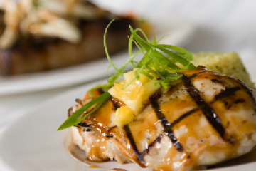 Grilled chicken with glaze and pineapple garnish on a white plate.