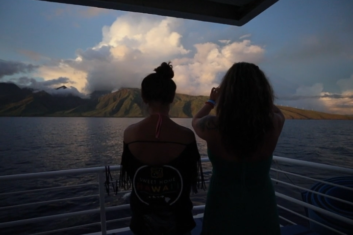 Two people on a boat looking at a mountain view during sunset.