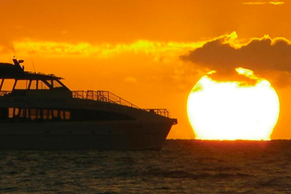 Silhouette of a boat against an orange sunset over the ocean.
