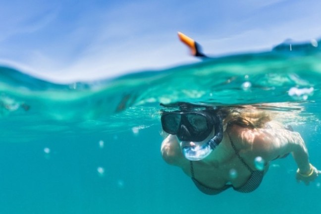 Person snorkeling underwater with a blue sky above the surface.