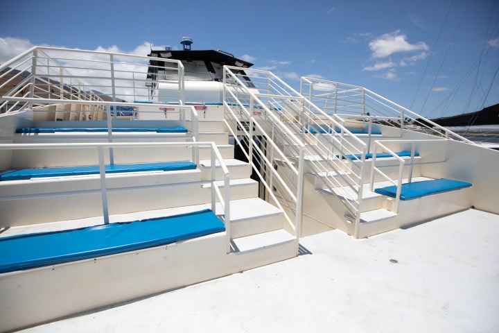 White boat deck with blue cushioned seats and metal railings under a clear sky.