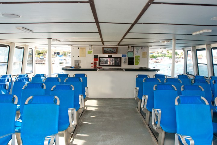 Interior of a ferry with rows of blue seats and windows on both sides.