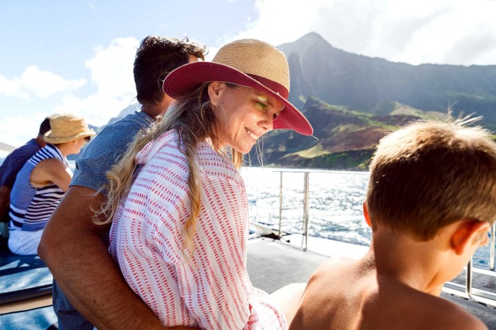People enjoying a sunny boat ride with mountains and ocean in the background.