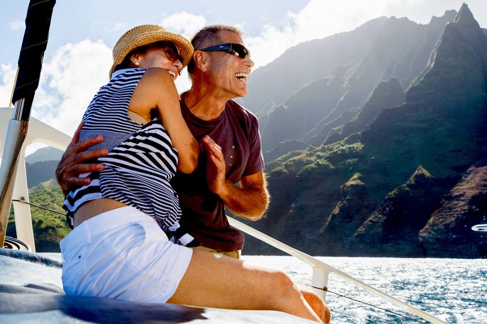 Smiling couple on a boat with scenic mountain background.