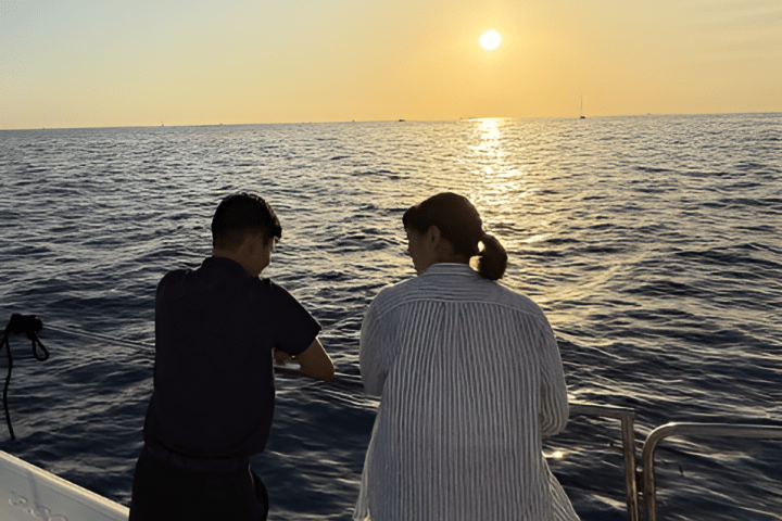 Two people on a boat watching sunset over the ocean.