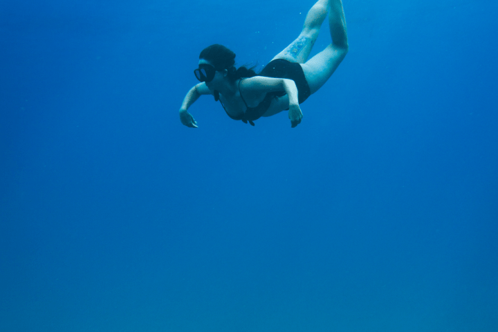 Person snorkeling underwater with flippers in clear blue ocean.