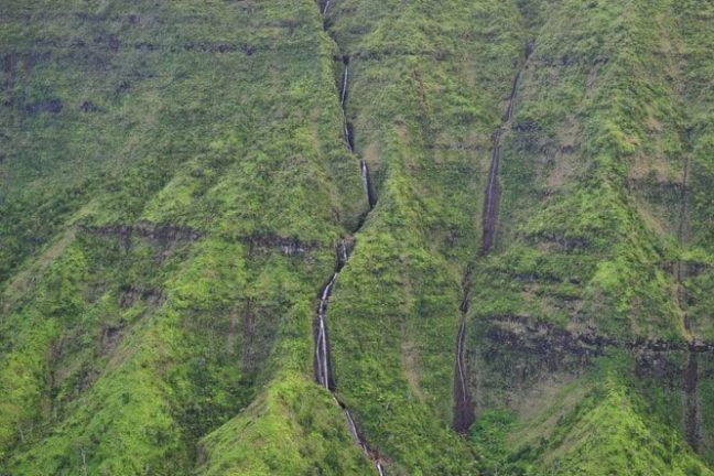 Tall waterfall cascading down a lush green mountain slope, shrouded in mist at the top.