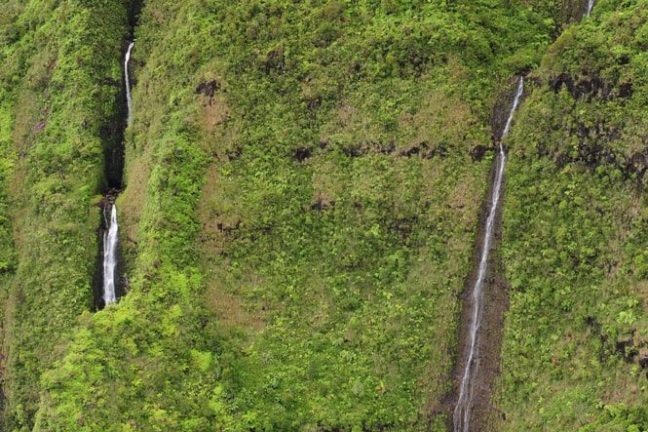 Lush green cliffs with three waterfalls cascading down the vegetation-covered rocks.