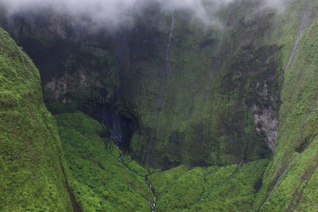 Aerial view of a lush green valley with a narrow river and waterfalls.