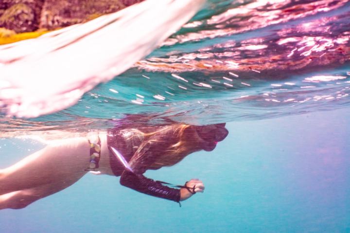 Person snorkeling underwater with rocky coastline in background.