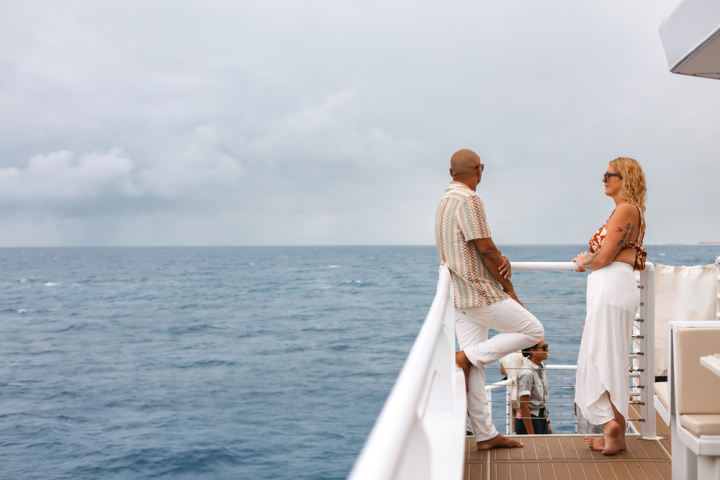 Two people standing on a ship deck, gazing at the ocean under a cloudy sky.
