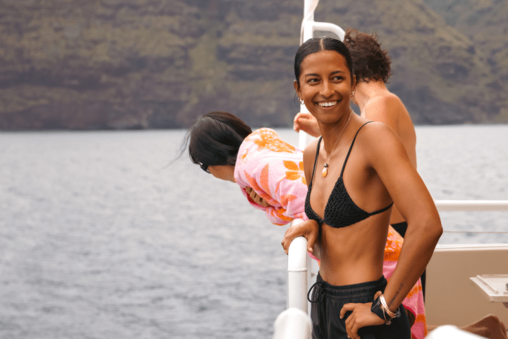 Smiling person on boat, others leaning over railing, mountain in background.