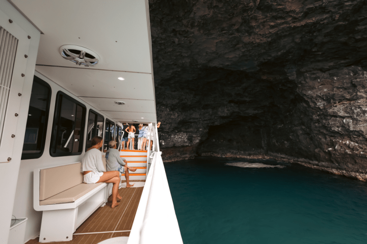 People on a boat near a rocky cave with turquoise water.