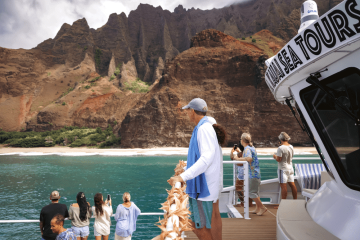 People on a boat tour admire steep cliffs and turquoise water.