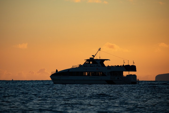 Silhouette of a boat on the ocean at sunset with an orange sky.