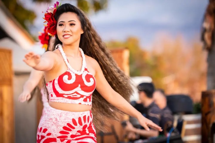 Woman in a red and white outfit performing a traditional dance outdoors, with a flower in her hair.