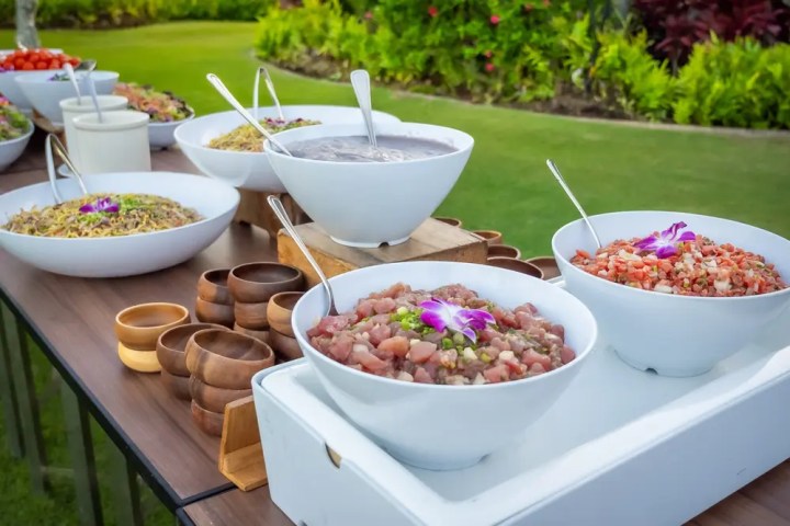 Outdoor buffet table with assorted dishes in white bowls, garnished with purple flowers.