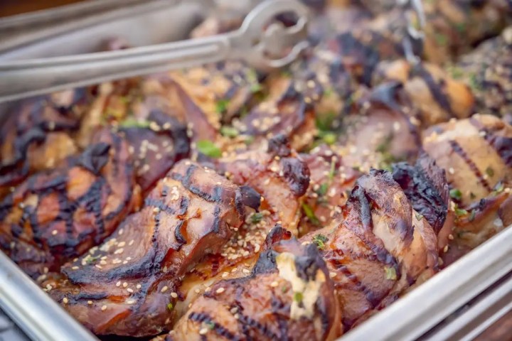 Grilled chicken pieces in a tray, garnished with sesame seeds and herbs.