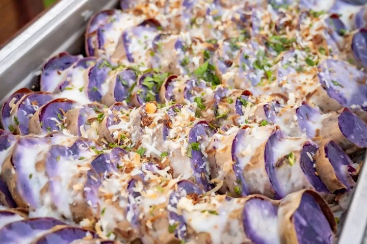 Sliced purple sweet potatoes with cream and herbs in a metal tray.