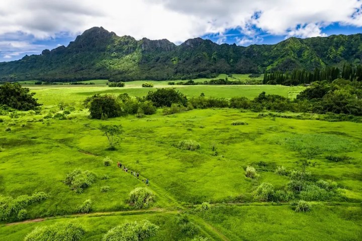Lush green valley with distant mountain range and cloudy sky.
