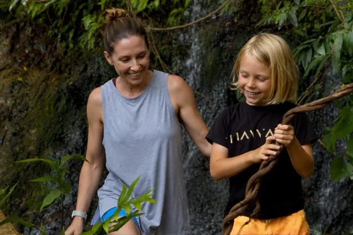 Smiling woman and child holding vine in lush greenery.