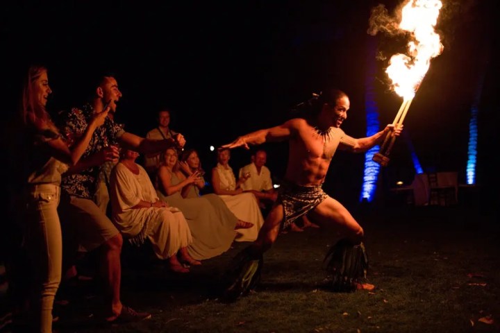 Fire performer dancing with lit torches before a cheering audience at night.