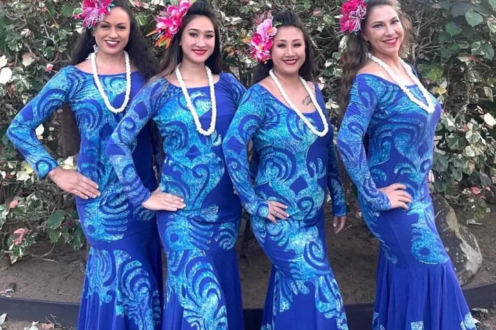 Four women in blue dresses with floral patterns and flower hair accessories.