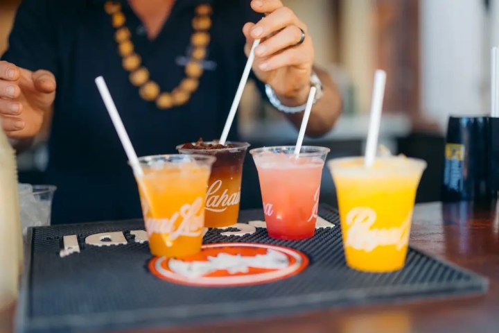 Person arranging colorful drinks with straws on a bar mat.