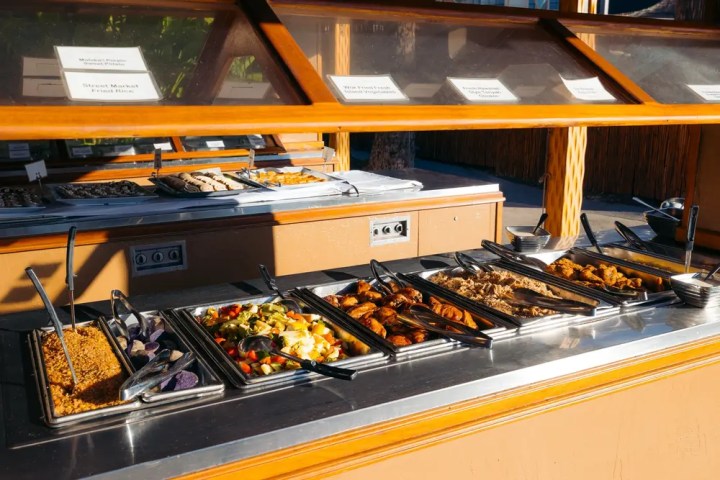 Buffet with trays of assorted foods under a glass cover.